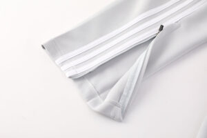 Close-up of light gray athletic pants leg with white side stripes and a zip at the cuff edge.