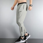 Side view of a person wearing light gray Nike joggers with black zip pockets and black sneakers with white soles.