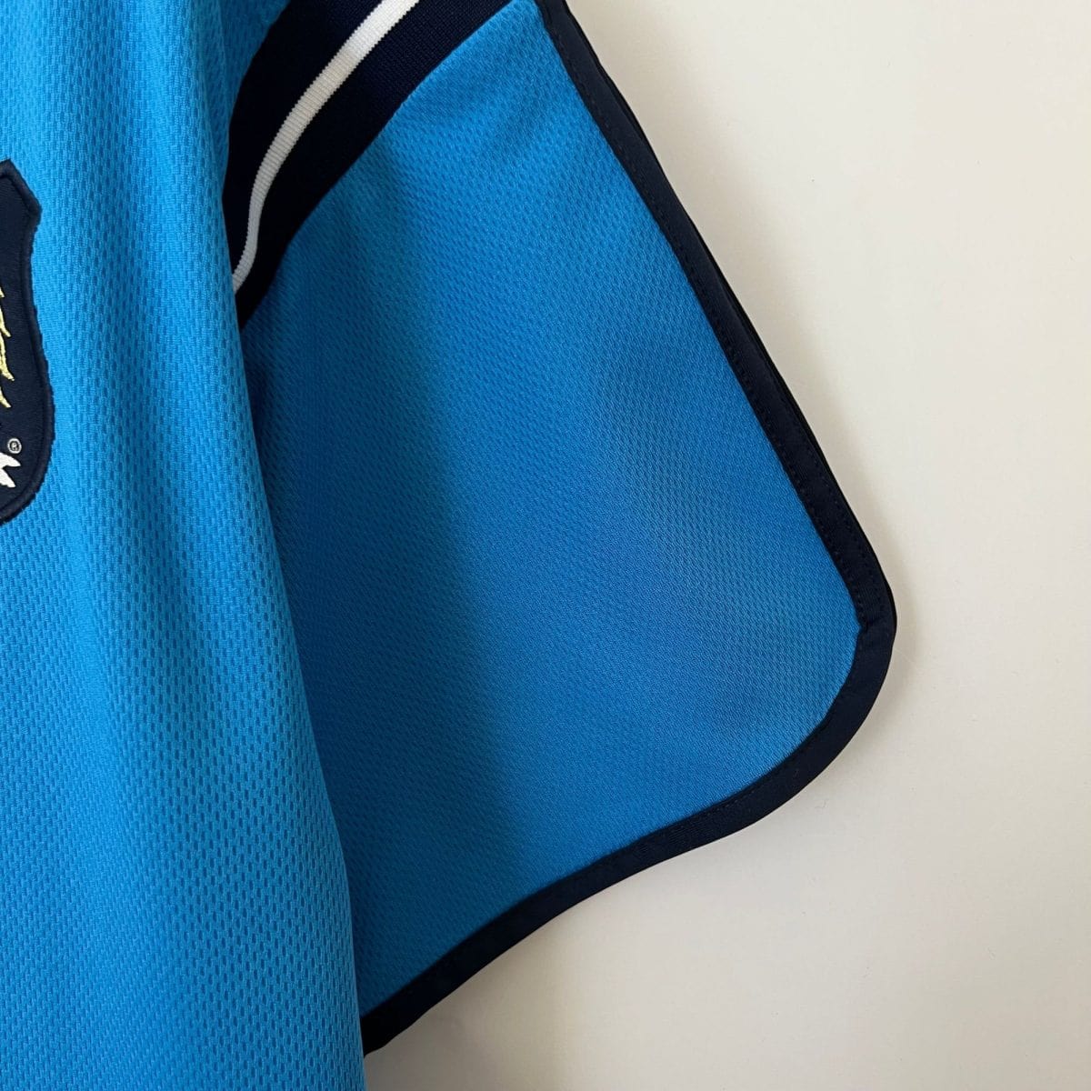 Close-up of bright blue mesh fabric with dark navy seam along the edge, suggesting a backpack or sportswear item.