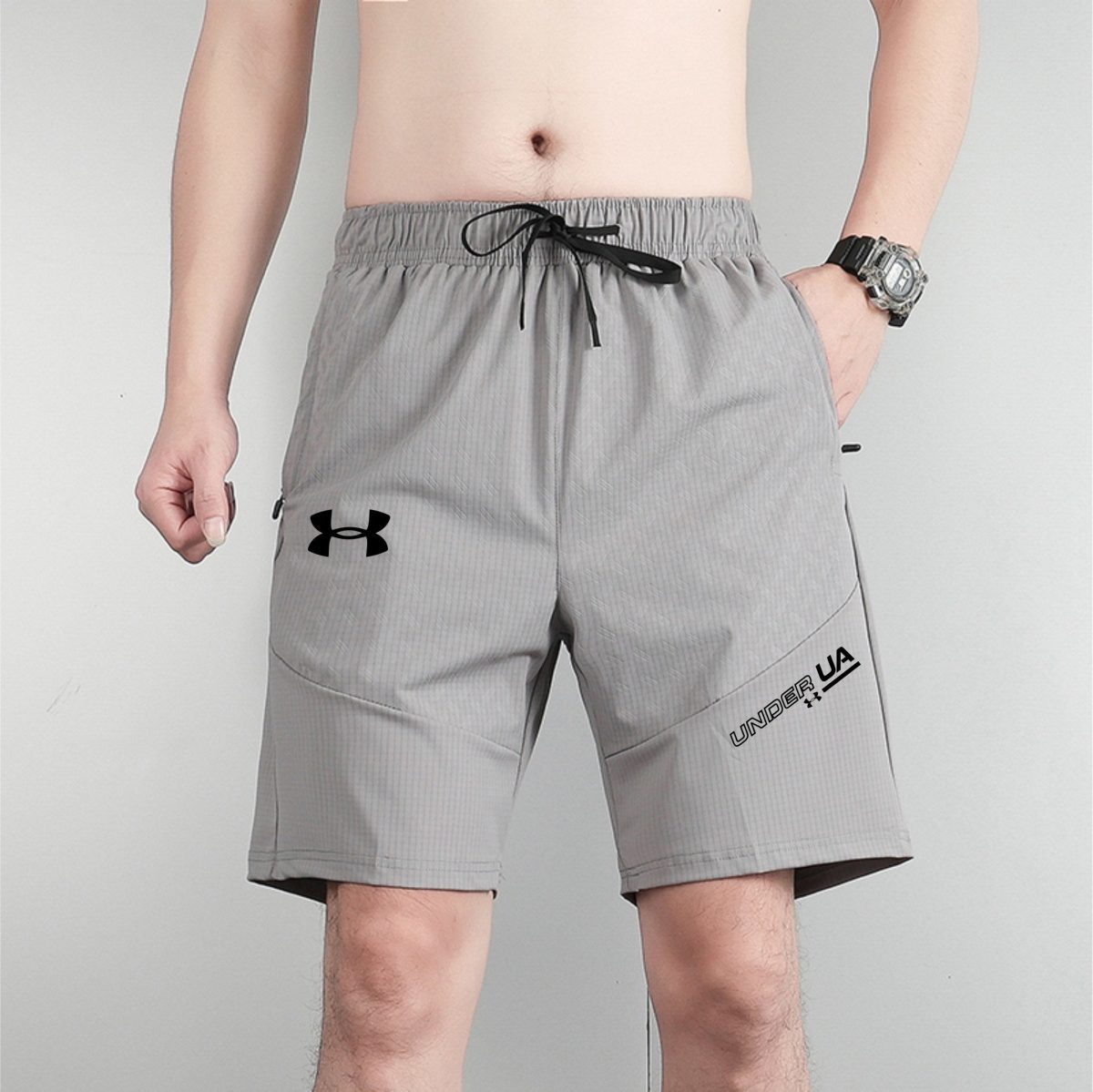 Man wearing gray athletic shorts with a black drawstring, standing with arms at his sides and wearing a silver wristwatch on the left wrist.