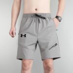 Man wearing gray athletic shorts with a black drawstring, standing with arms at his sides and wearing a silver wristwatch on the left wrist.