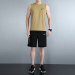 Man wearing a tan sleeveless Nike top and black Nike Pro shorts, standing against a plain backdrop.