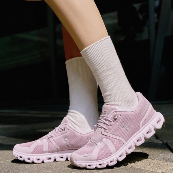 Woman wearing light pink athletic sneakers and white crew socks, standing on a sunlit pavement.