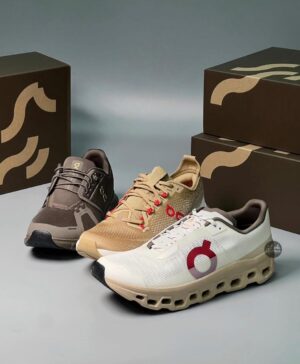 Three On running sneakers in black, tan, and white, arranged in front of product boxes on a neutral surface.