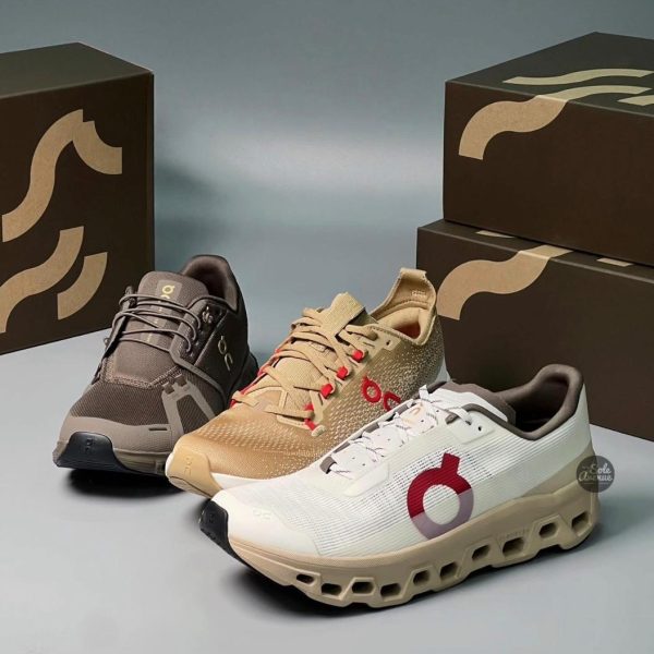 Three athletic sneakers in black, tan, and white, with perforated uppers, shown on a light gray surface beside dark shoeboxes.