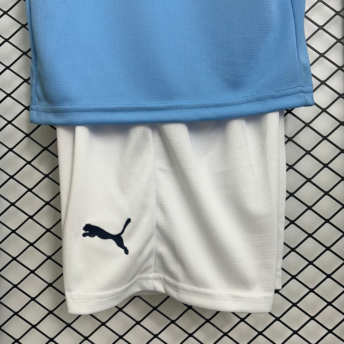 Close-up of blue athletic fabric laid over a white garment with a navy Puma logo, on a black grid background.