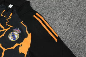 Close-up of a Real Madrid football jersey: black with orange camouflage pattern and the club crest on the chest area, orange stripes on the sleeve.