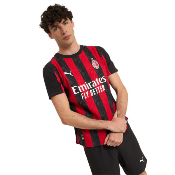 Young man posing in a red-and-black AC Milan football jersey with arms crossed, against a white background.