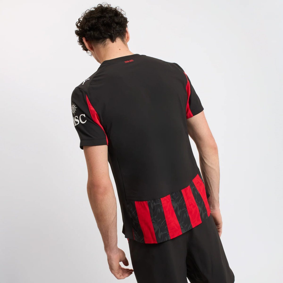 Back view of a man in a black athletic jersey with red vertical stripes along the sides and patterned hem, against a light background.