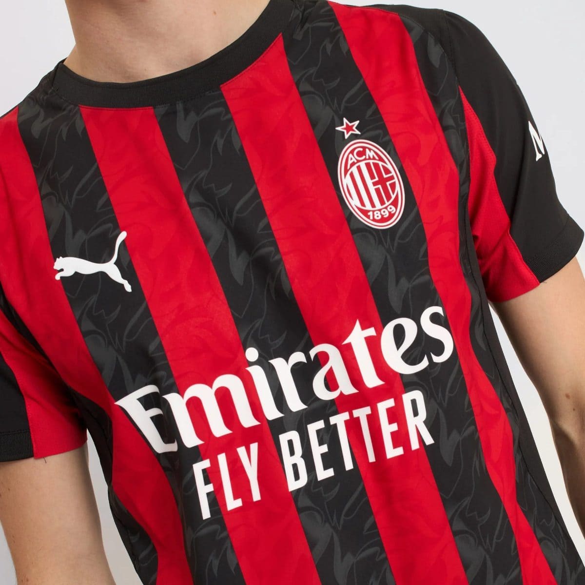 Close-up of an AC Milan football jersey with red and black stripes, club crest, and white Puma logo.