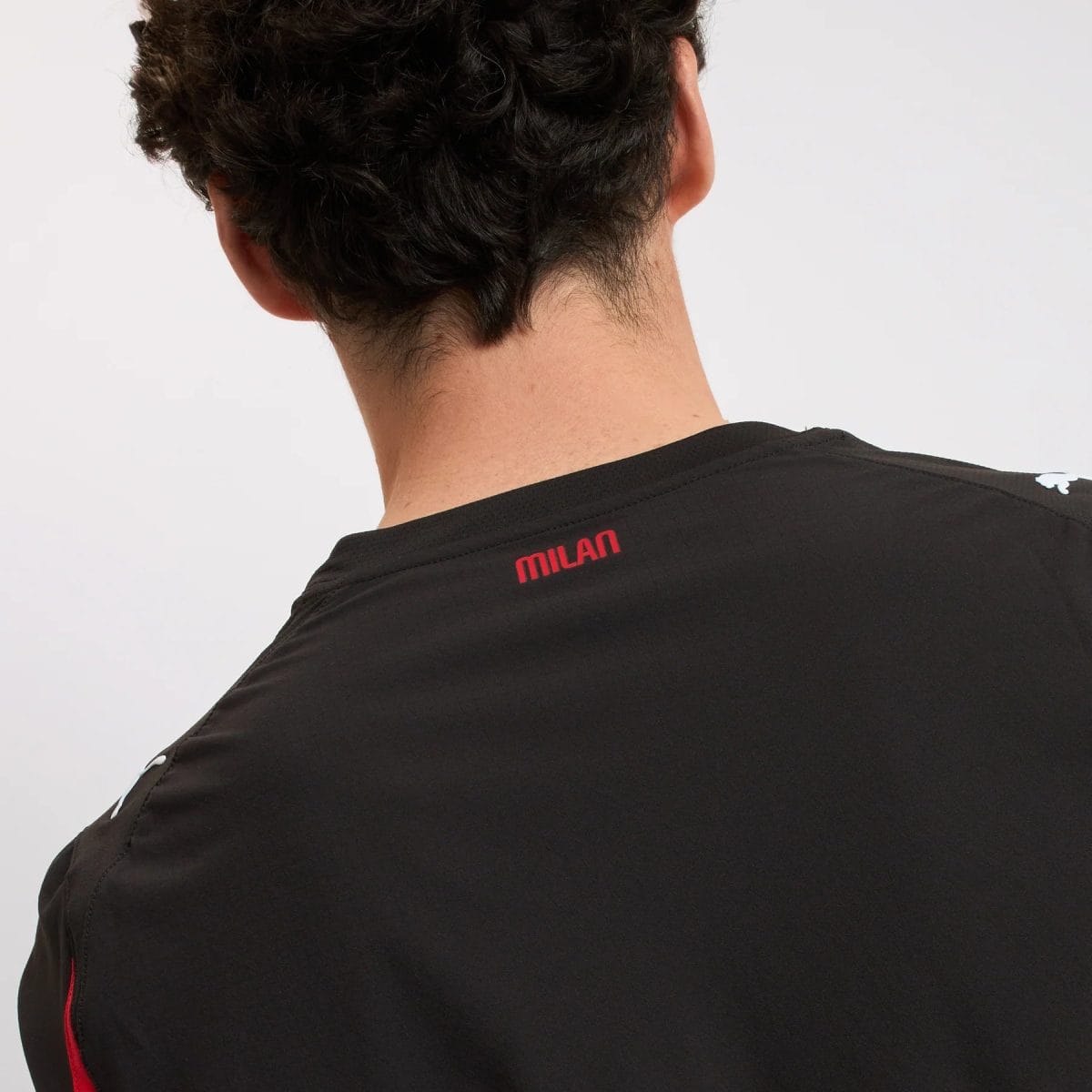 Back view of a person wearing a black athletic shirt with a red MILAN logo on the back neck area.