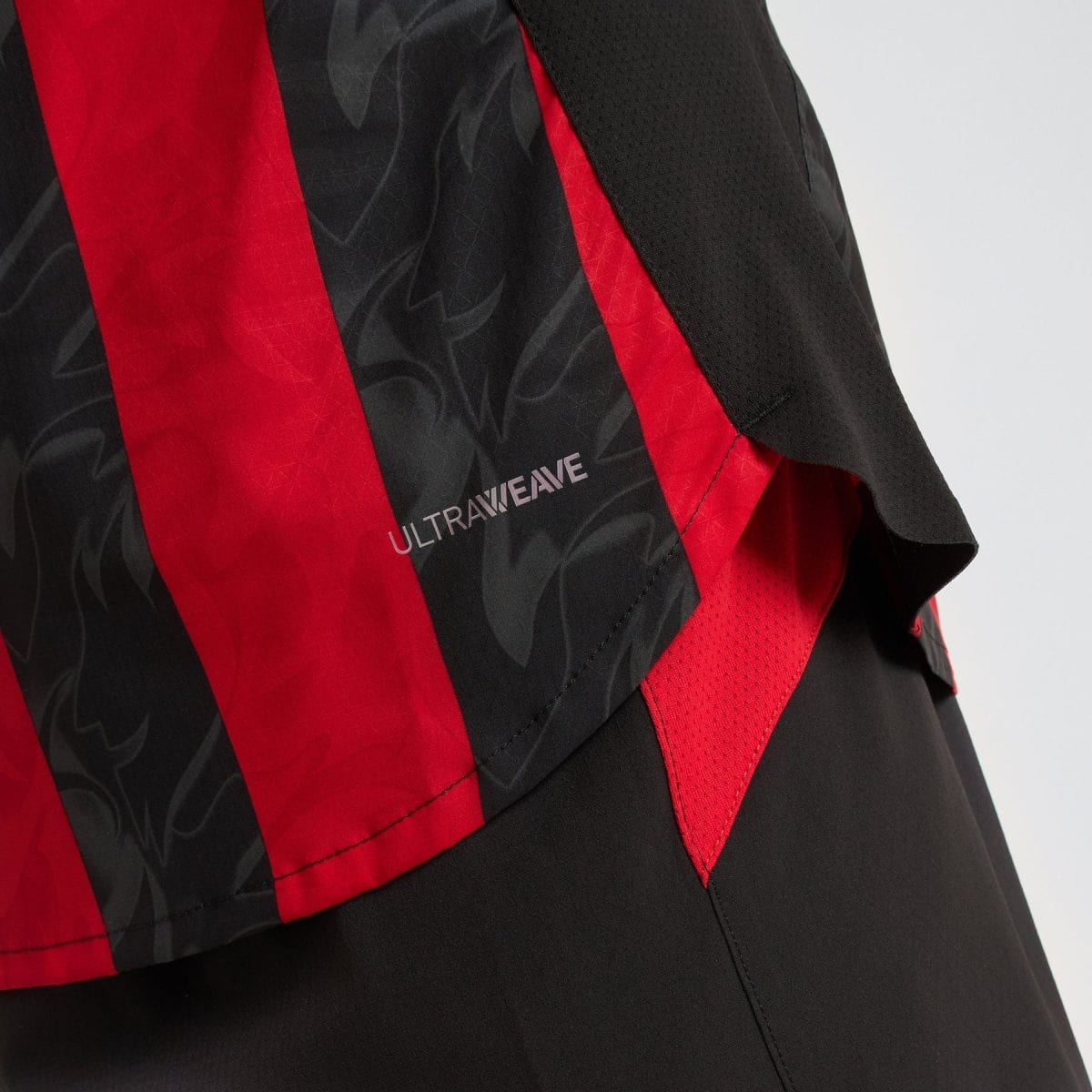 Close-up of a black and red sports jacket with a diagonal red stripe and subtle pattern; faint 'ULTRAWAVE' logo visible.