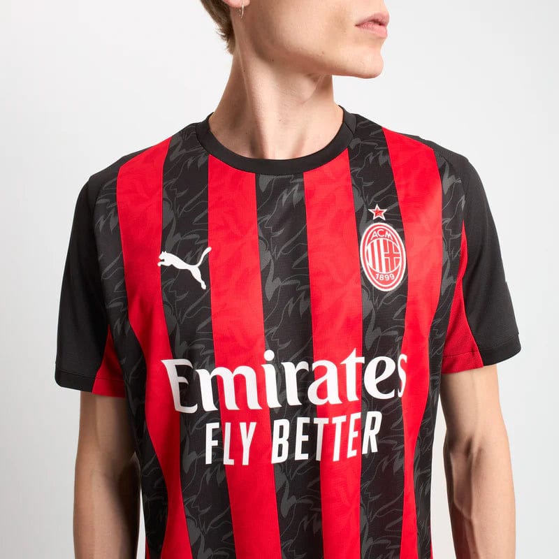 779962-A81_06_800x_24c3db0c-13d3-43d1-86f1-0e288f2e8815 | UAE SPORT STORE Person wearing an AC Milan home football jersey with red and black vertical stripes and Emirates Fly Better sponsor text across the chest.