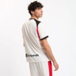 Man wearing a white sports jersey with black and red accents, facing away, brand 'bitpanda' on the lower back side.