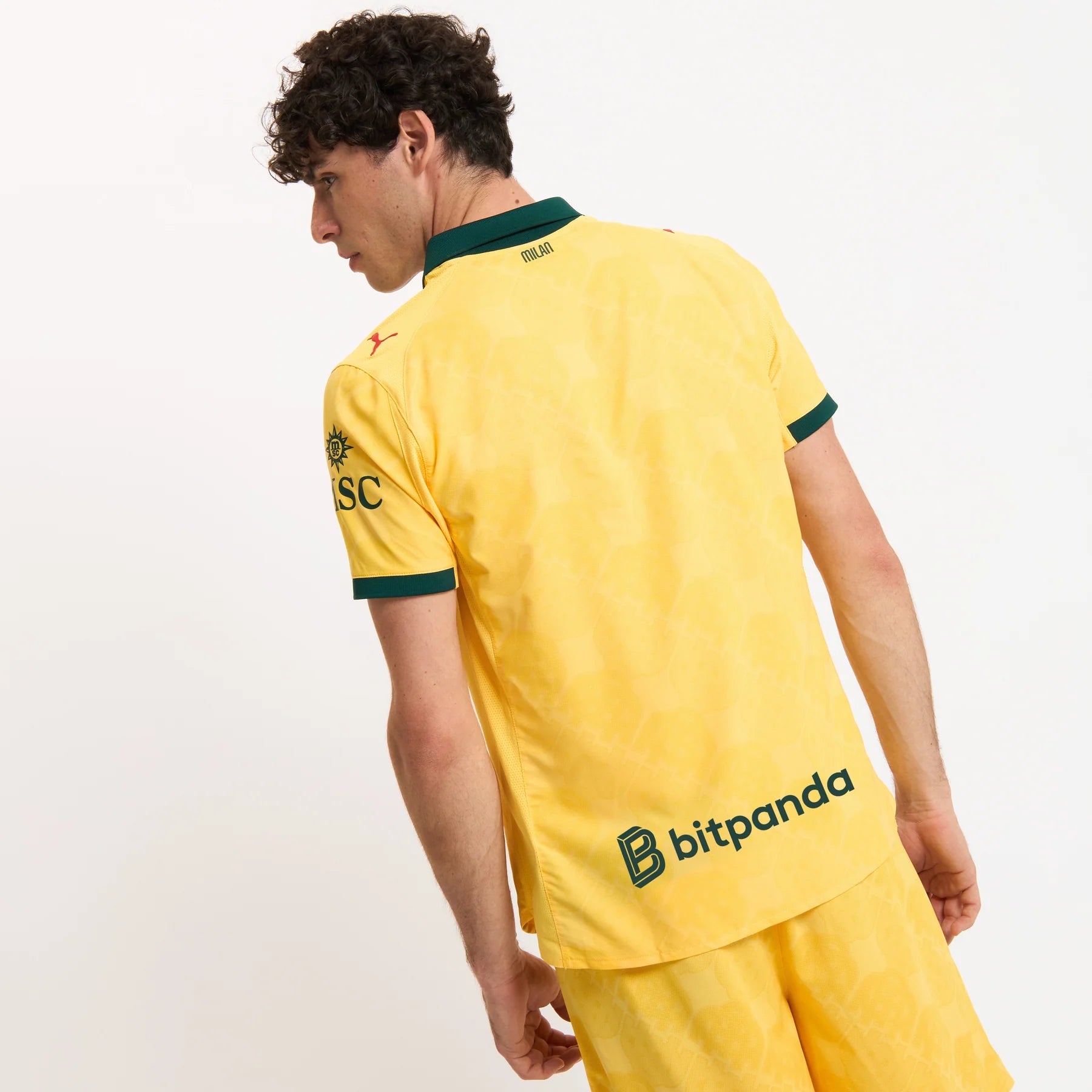 779978-C22_05_1800x1800_8adae110-734d-4604-9e4b-7925cc450d3d | UAE SPORT STORE Back view of a man in a yellow soccer jersey with a green collar; logos and text appear on the back and sleeve.