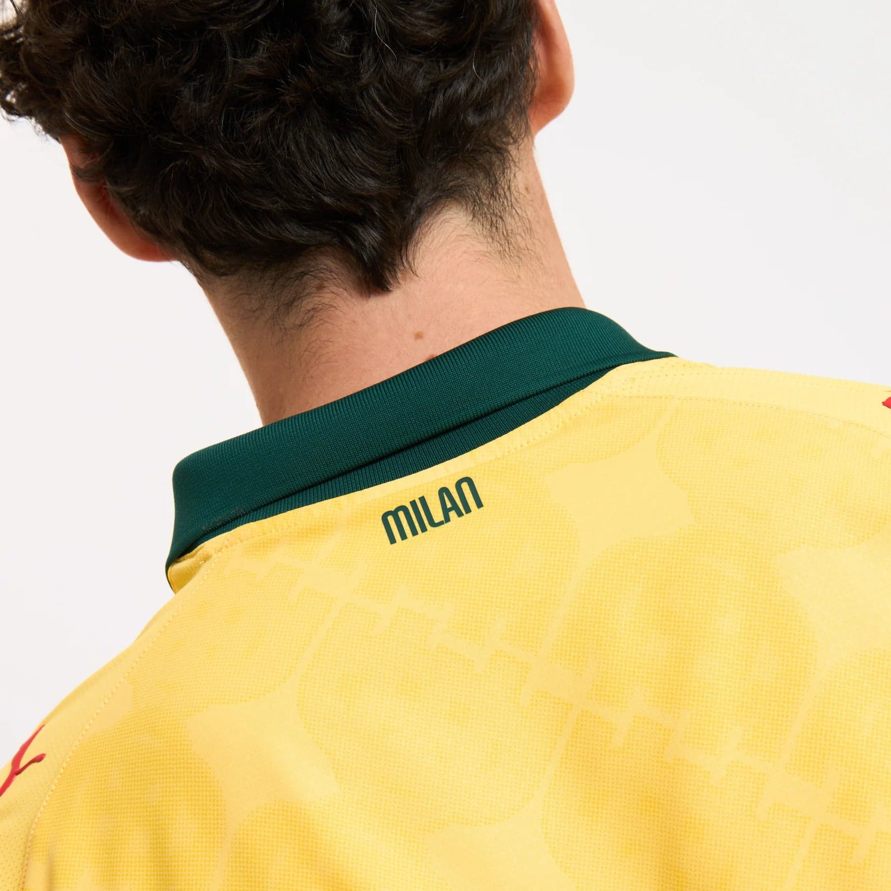 779978-C22_08_1800x1800_54da7572-b337-44de-ad92-a2d3284af130 | UAE SPORT STORE Back of a person wearing a yellow sports jersey with a dark green collar; the word 'MILAN' appears on the back edge of the collar area.
