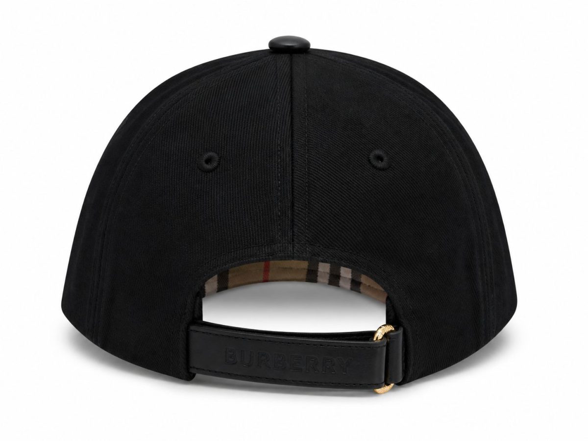 Black baseball cap shown from the back, with a Burberry leather strap and gold buckle; plaid lining peeks through the opening.