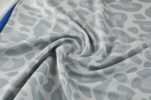 Light gray fabric with irregular blue-gray abstract spots, gently folded and textured.