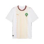White football jersey with a gold geometric pattern, red-green collar, and a green circular team crest on the chest.