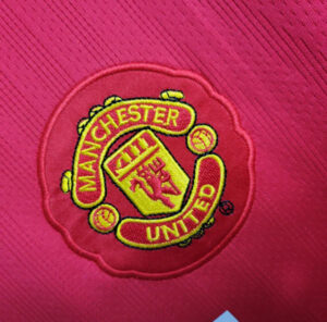 Embroidered Manchester United crest on pink fabric.