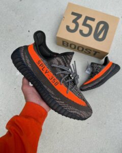 Pair of dark gray and orange Adidas Yeezy Boost 350 sneakers, one being held up with a beige 350 box in the background.