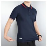 Navy polo shirt with red trim on collar and sleeve cuffs worn by a man; chest logo visible.