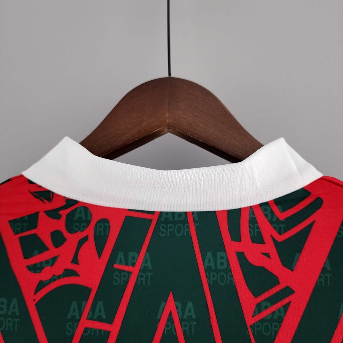 Close-up of a white polo collar on a wooden hanger, with a red and dark green printed garment featuring bold diagonal text on the fabric.