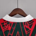 7907767b_5341185b-b9ec-489a-9a58-2b18c51e1800 | UAE SPORT STORE Close-up of a white polo collar on a wooden hanger, with a red and dark green printed garment featuring bold diagonal text on the fabric.