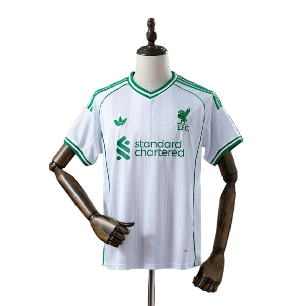 White Liverpool FC football jersey on a mannequin, green trim and sponsor logo 'standard chartered' visible