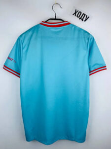 Light blue sports jersey on a hanger with red and white striped collar and sleeve cuffs on both arms.