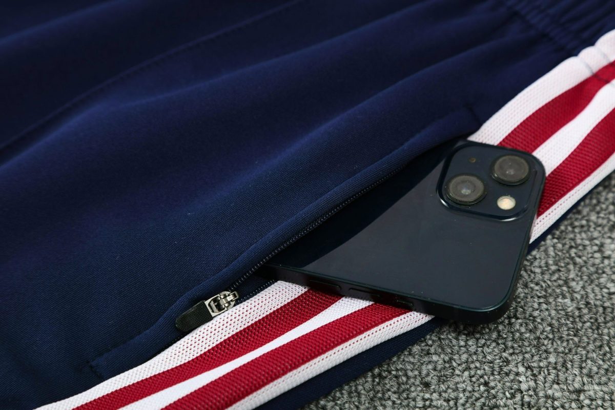 Close-up of a navy backpack zipper with a black smartphone showing dual cameras resting on a red-and-white striped strap.