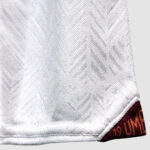Close-up of white fabric with a chevron-like weave and a burgundy tag at the hem showing 'UM' (partial).