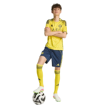 Young male soccer player in a yellow jersey and blue shorts with one foot on a soccer ball.