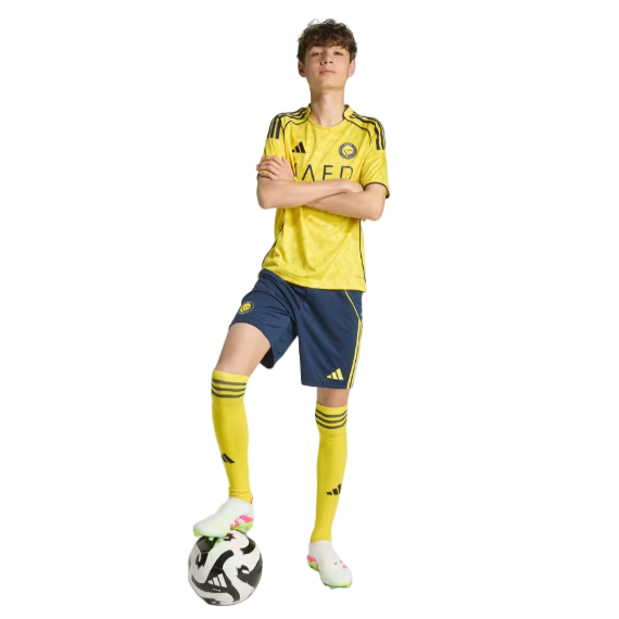 Young male soccer player in a yellow jersey and blue shorts with one foot on a soccer ball.