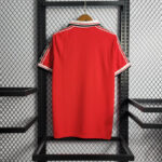 Red polo shirt with white and black striped collar on a wooden hanger in a black metal rack.