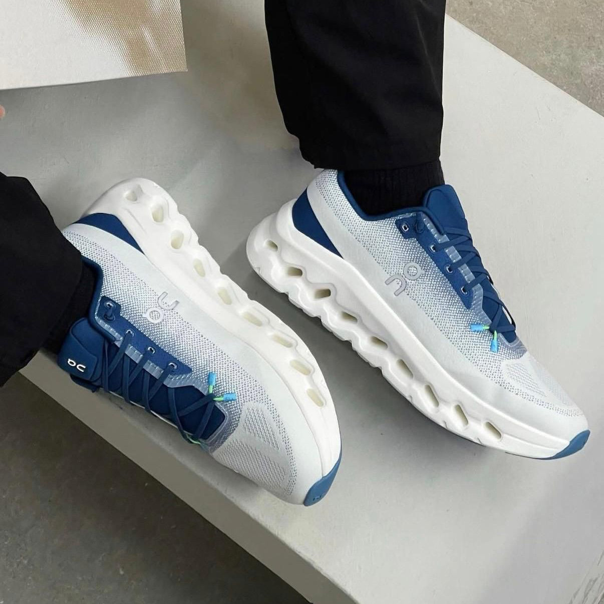 7a08c2b5-dc81-452e-bc27-75553e0a9d69 | UAE SPORT STORE White and blue On running sneakers with a segmented hollow midsole, worn by a person in black pants.
