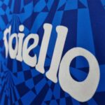 Close-up of blue geometric-patterned fabric with white cursive letters forming part of a logo on a jersey.