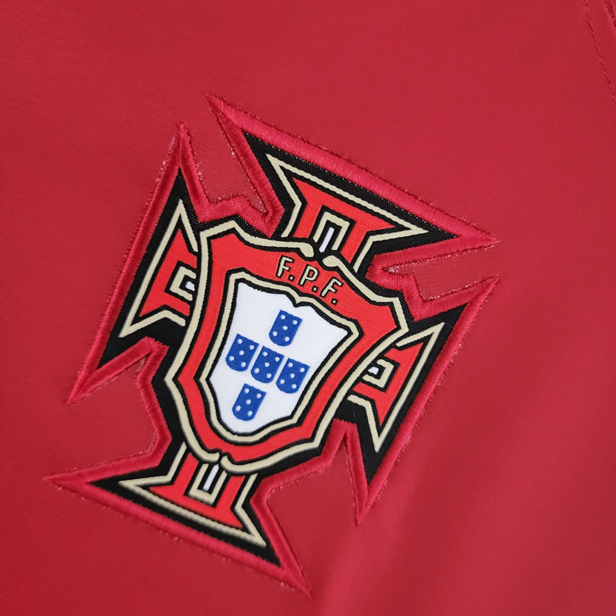 7a5c3832_afae616c-5839-42b2-8513-e3d5ef492795 | UAE SPORT STORE Close-up of a red leather patch with a shield-shaped emblem and blue dice against a red background.