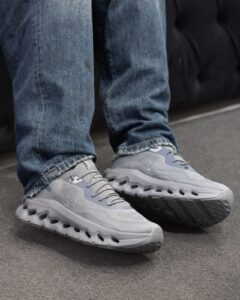 Close-up of gray running shoes on a person wearing blue jeans, standing on a paved surface.