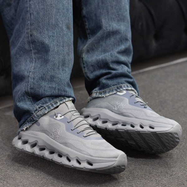 Close-up of gray running shoes on a person wearing blue jeans, standing on a paved surface.