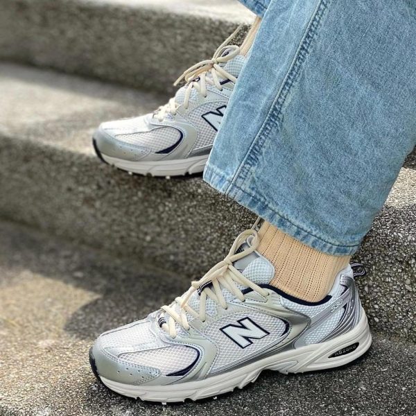 Close-up of light gray New Balance sneakers on concrete steps, with beige socks and denim jeans visible.
