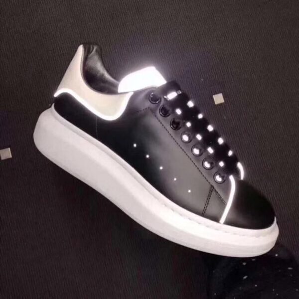 Black sneaker with a thick white sole and LED-lit laces, viewed from side. Reflective white trim along heel and toe area.