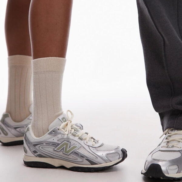 Close-up of legs in beige socks and silver athletic sneakers, standing side by side on a light background.