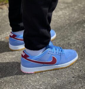 Blue Nike sneakers with a maroon swoosh, white socks, and black pants standing on a pavement surface.