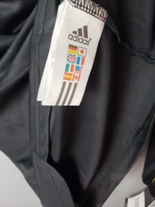 White Adidas tag showing the logo and a grid of small national flags on a black garment.