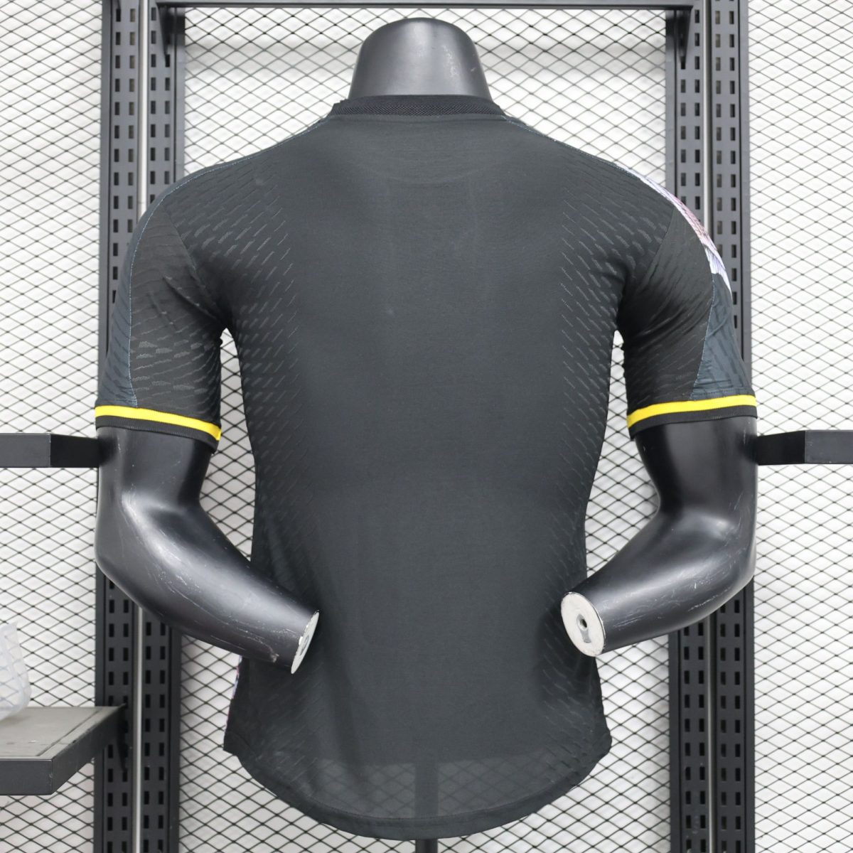 Mannequin torso wearing a black athletic shirt with yellow sleeve trim, displayed on a metal rack with a grid background.