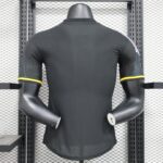 Mannequin torso wearing a black athletic shirt with yellow sleeve trim, displayed on a metal rack with a grid background.