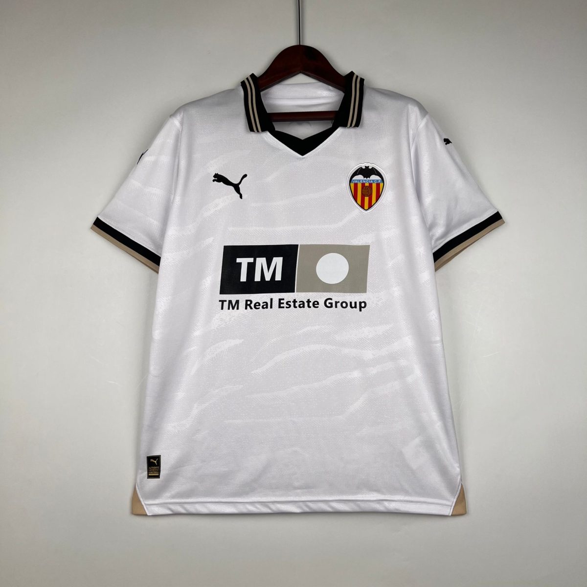 White Valencia CF football shirt on a wooden hanger, with a black-trimmed collar and TM Real Estate sponsor logo visible on the chest area.