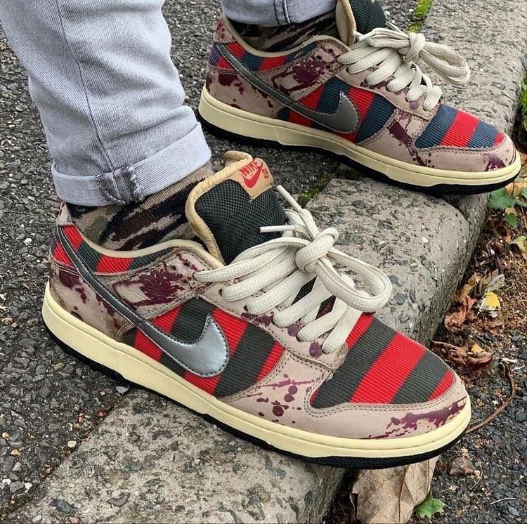 7bb7ab00-7339-4d88-bee9-17ec796954b6 Multi-color Nike sneakers with red stripes and camouflage patches resting on a concrete step.