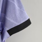 Close-up of lavender knit fabric with a black elastic band running diagonally across the frame, showing texture and stitching detail under bright light.